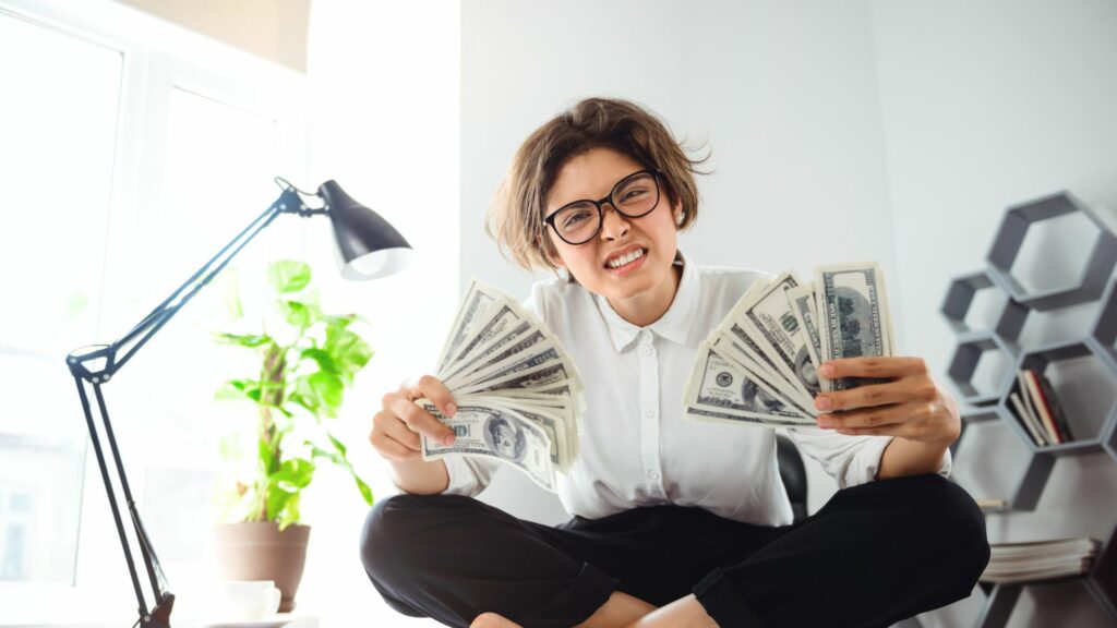 A girl overwhelmed, sitting on a table holding her for passive income money in her hands