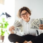 A girl overwhelmed, sitting on a table holding her for passive income money in her hands