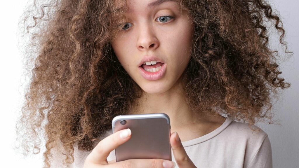 A girl shocked by reading trending headlines on Baddienews website on her phone