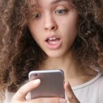 A girl shocked by reading trending headlines on Baddienews website on her phone