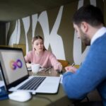 A man and woman collaborate at a table with a laptop, discussing in-house development versus outsourcing for business strategies.