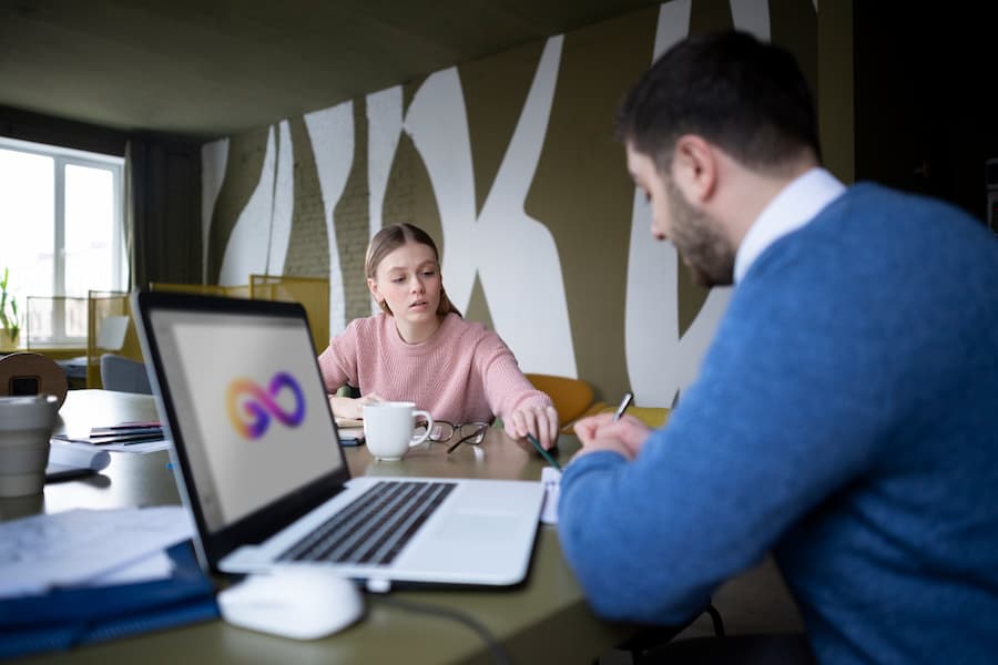 A man and woman collaborate at a table with a laptop, discussing in-house development versus outsourcing for business strategies.