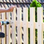 A man drills into wood to install a fence, using countersunk coach screws for secure attachment.