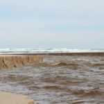 A sand dune erodes as ocean waves crash against it, highlighting the riverbank collapse at Iford Playing Fields.riverbank collapse iford playing fields