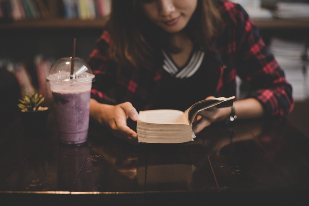 A woman reading a book at a table, with a drink beside her, in a cozy setting at Babeltee.