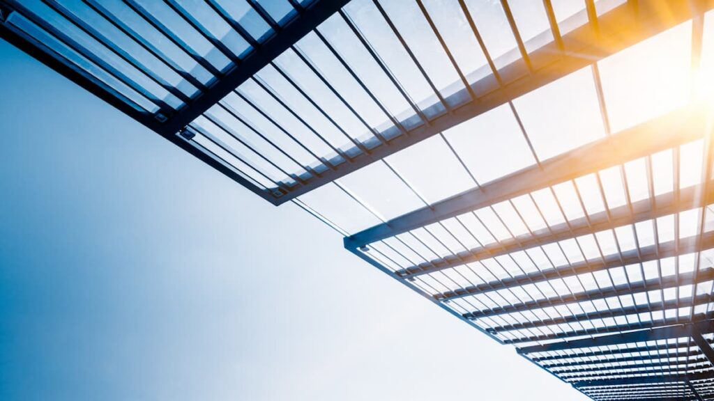 A metal structure with sunlight streaming through, highlighting its design and the surrounding environment. acryldach