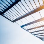 A metal structure with sunlight streaming through, highlighting its design and the surrounding environment. acryldach