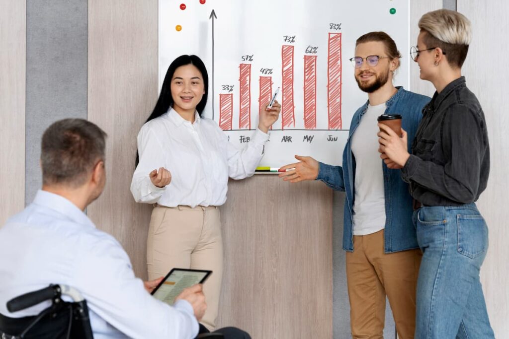 Three individuals standing by a whiteboard, analyzing a chart together in a professional setting. gldyql