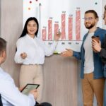 Three individuals standing by a whiteboard, analyzing a chart together in a professional setting. gldyql