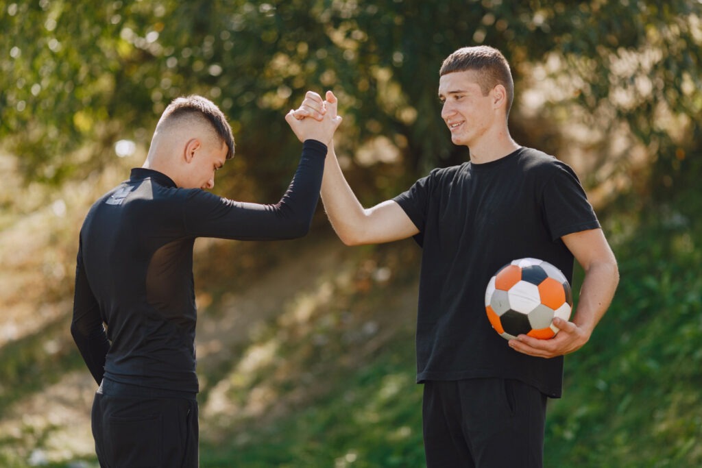 Two young men giving each other a high five while holding a soccer ball, celebrating a successful play together bảce