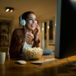 A woman wearing headphones enjoys a movie on her computer while eating popcorn, with the Flixfare logo visible